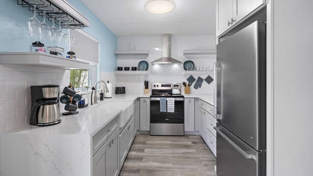A compact kitchen with white cabinets, a stainless steel refrigerator, a built-in oven, and a coffee maker.