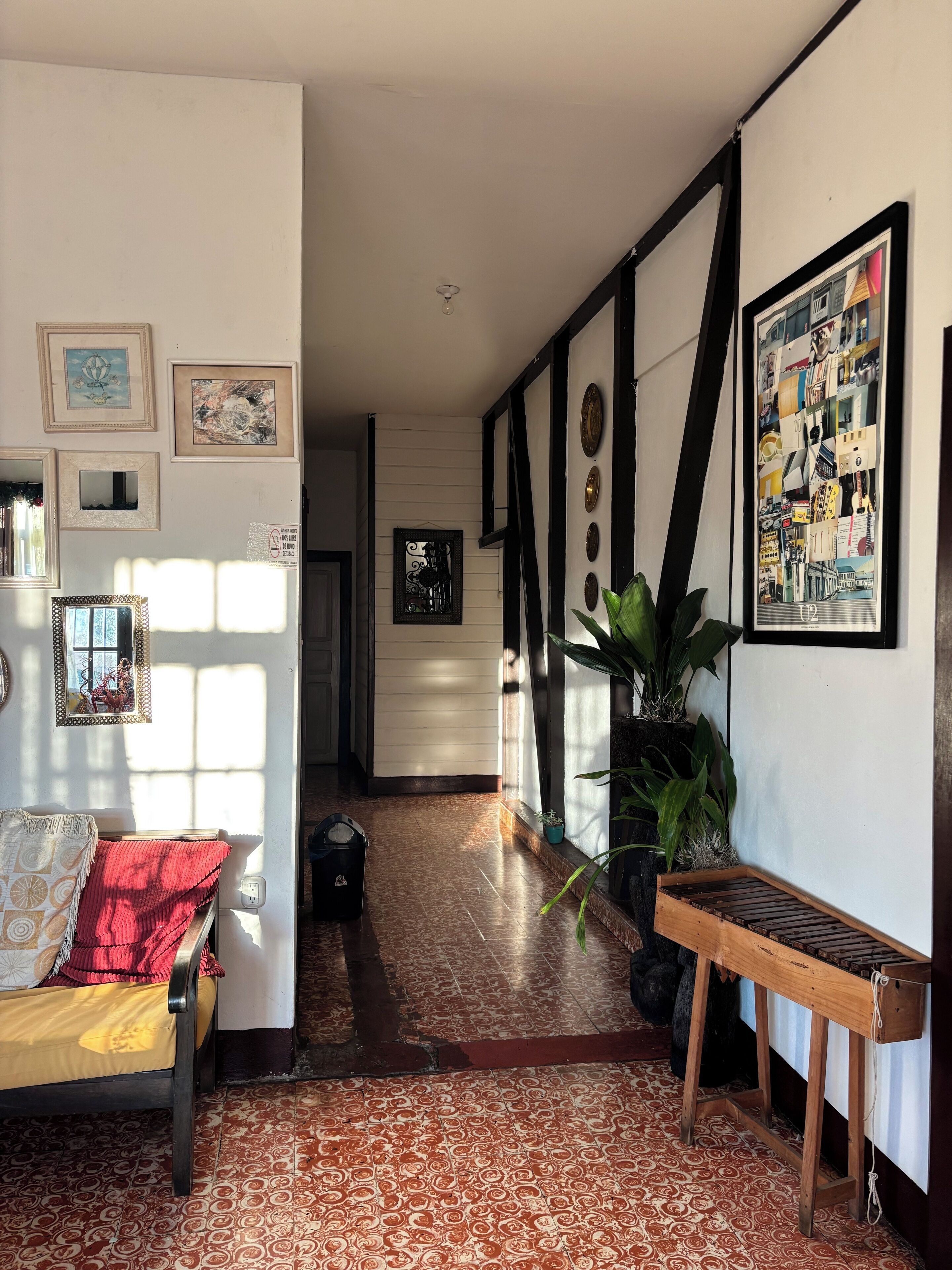 A hallway with a patterned floor, a bench, a red blanket on a sofa, and various framed pictures on the walls.
