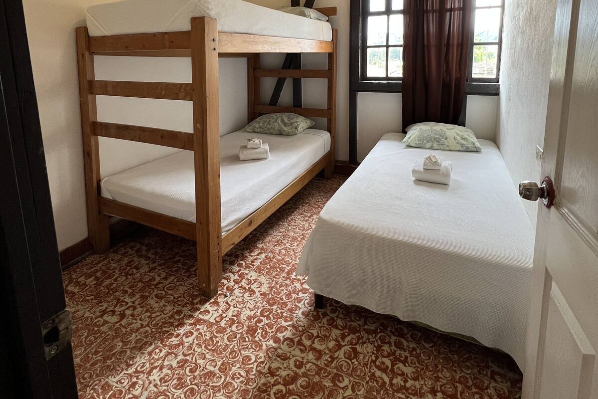 Une chambre avec un lit superposé, un lit simple, une moquette à motifs et une fenêtre avec des rideaux.