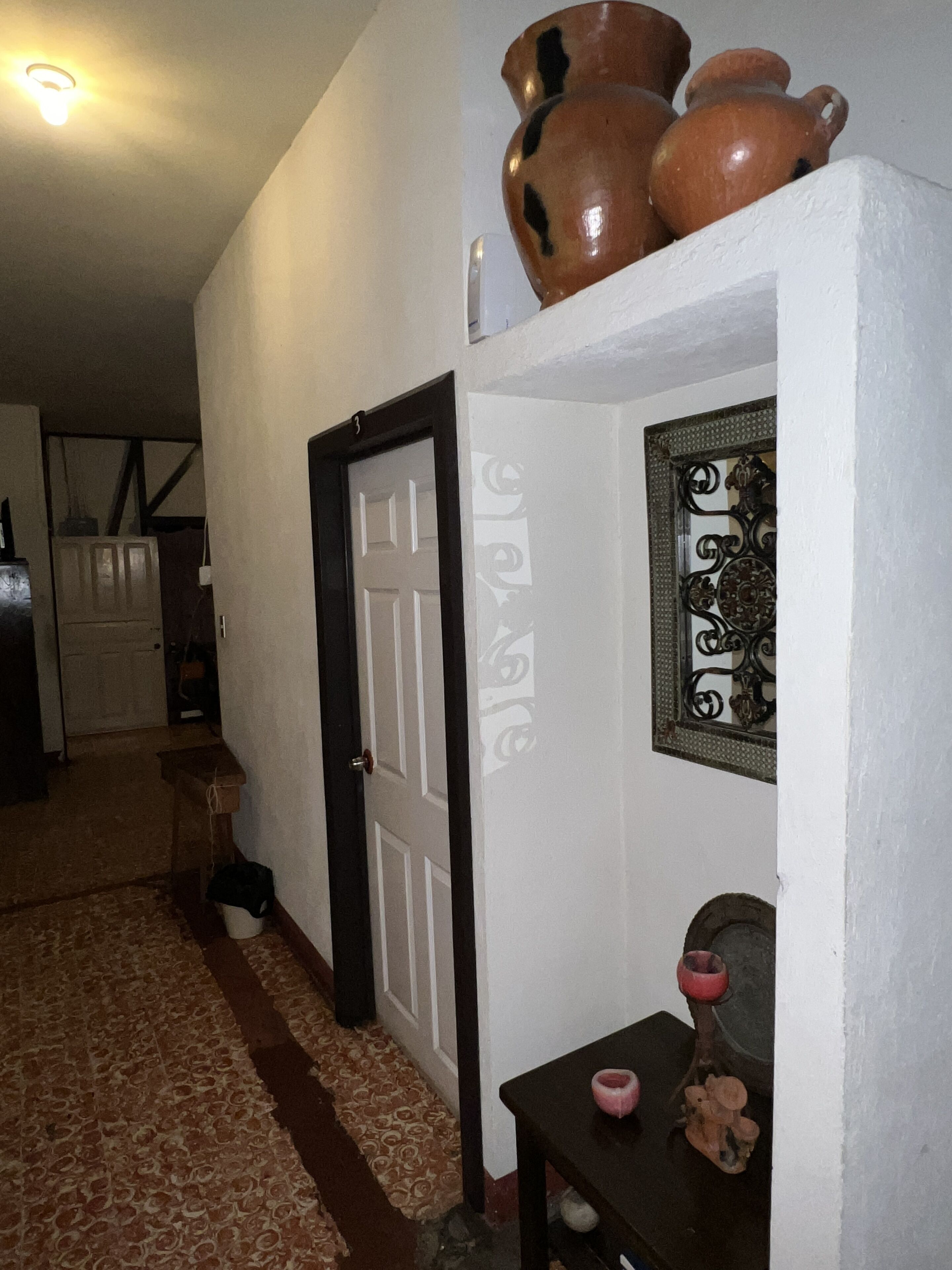 Un corridoio con una porta bianca, uno specchio decorativo e un tavolino con un oggetto rosa.