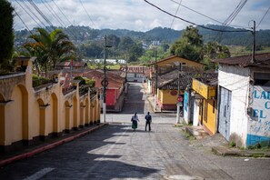 A street with buildings, a woman and a man walking, and a view of hills in the distance. - Hotel Casa Semuc (Cobán)