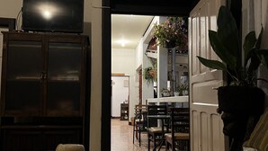 Una sala de estar con un sofá, una mesa de comedor y sillas. Hay un televisor sobre un mueble bajo, y un cuadro en la pared.