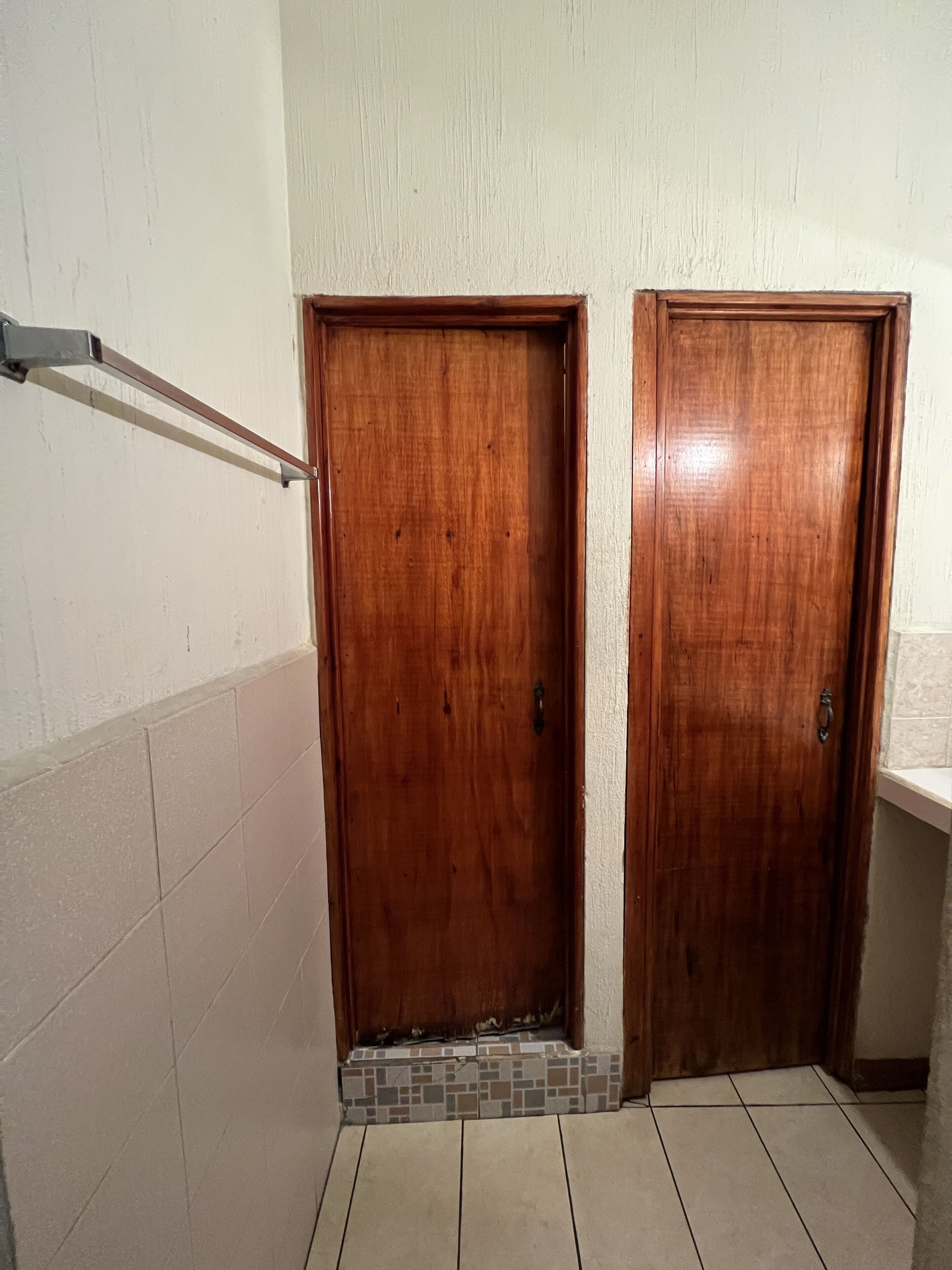 A hallway with two wooden doors, a tiled floor, and a metal handrail.