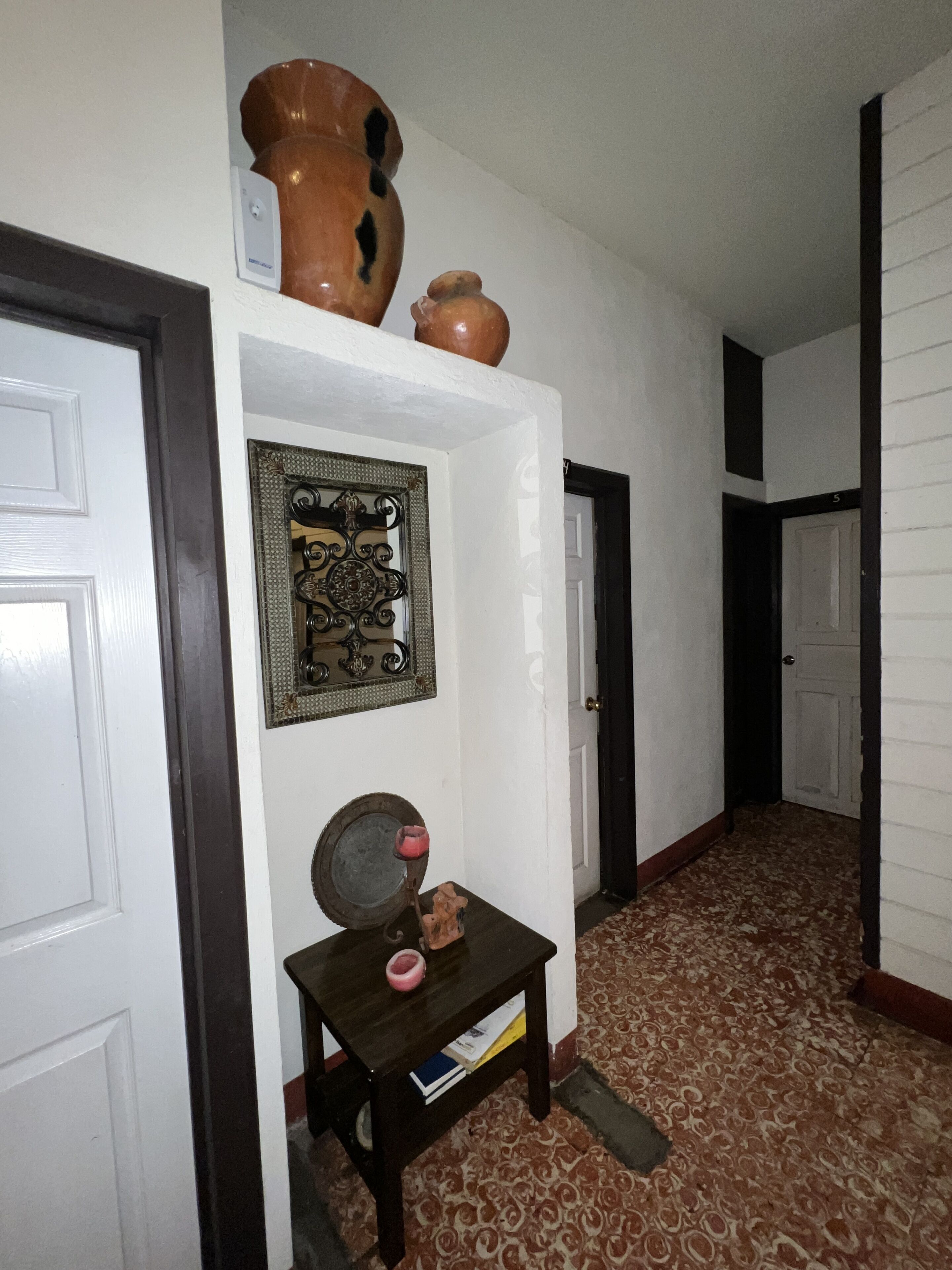 Un pasillo con piso estampado, una pequeña mesa con una vela y un adorno de pared.