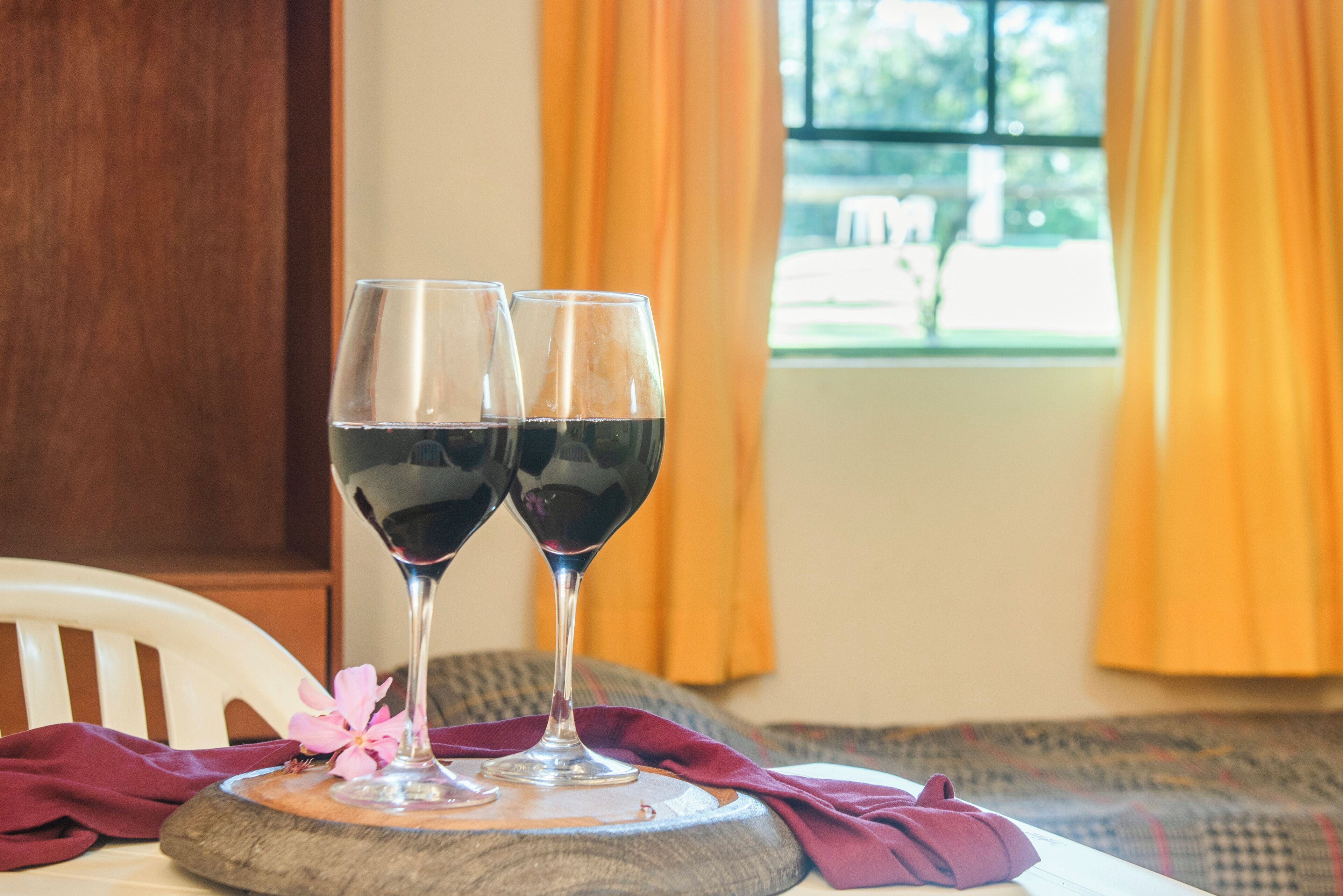 Two wine glasses on a wooden coaster with a cloth napkin, set on a white chair.