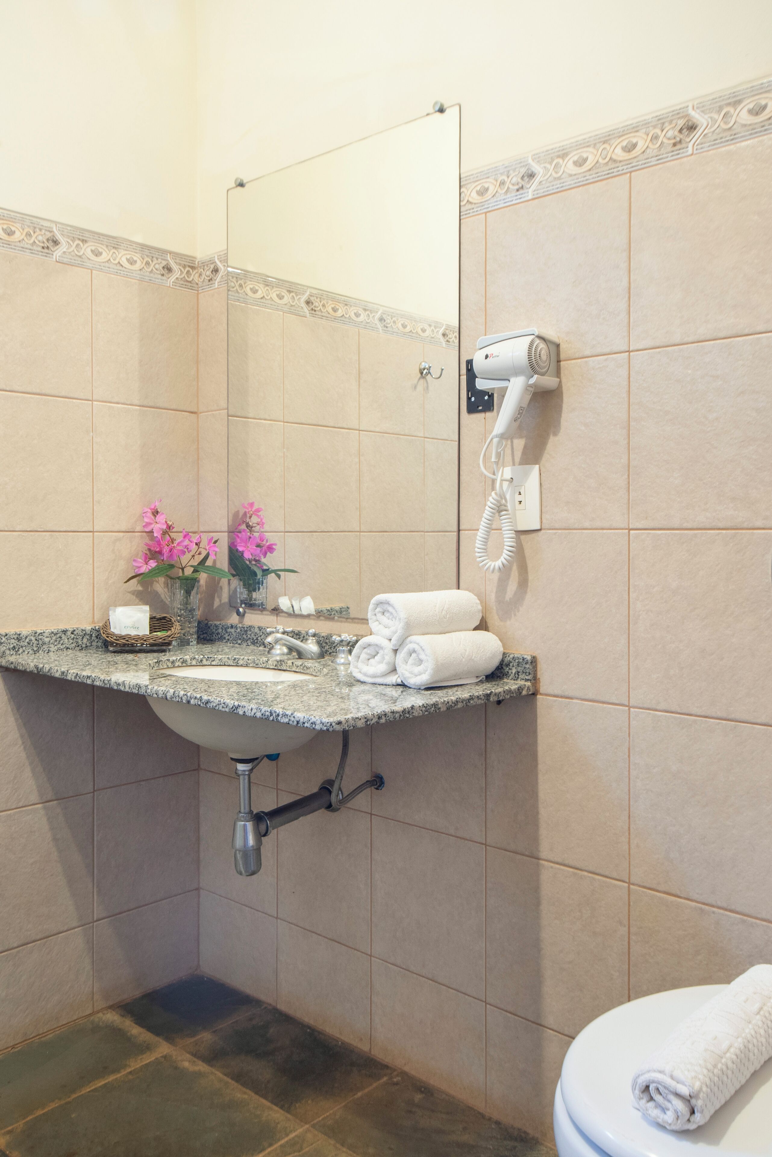 Un baño con lavamanos, espejo, toallero y secador de pelo en la pared.