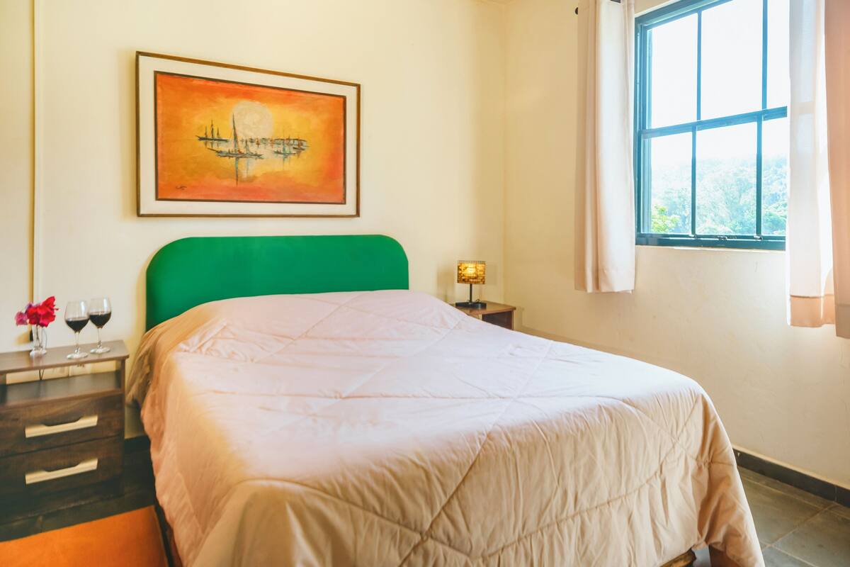 Un llit ben fet amb un reposacabeças verd, un quadre emmarcat a la part superior i una finestra amb cortines.