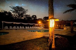 Area piscina con poltrone relax, una tenda e cielo stellato.