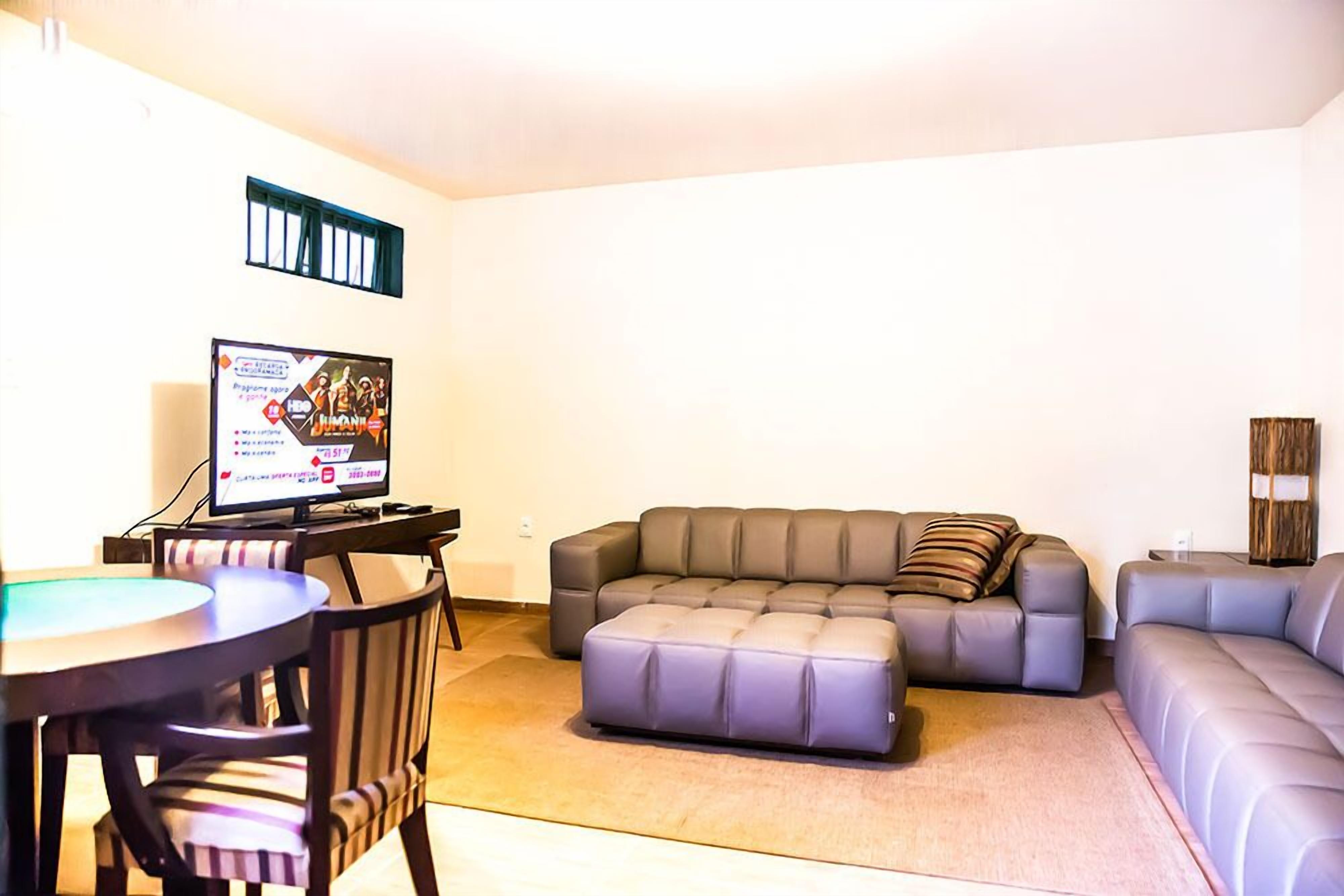 A living room with a grey sofa, a matching ottoman, a striped armchair, and a small table. A television is mounted on the wall.