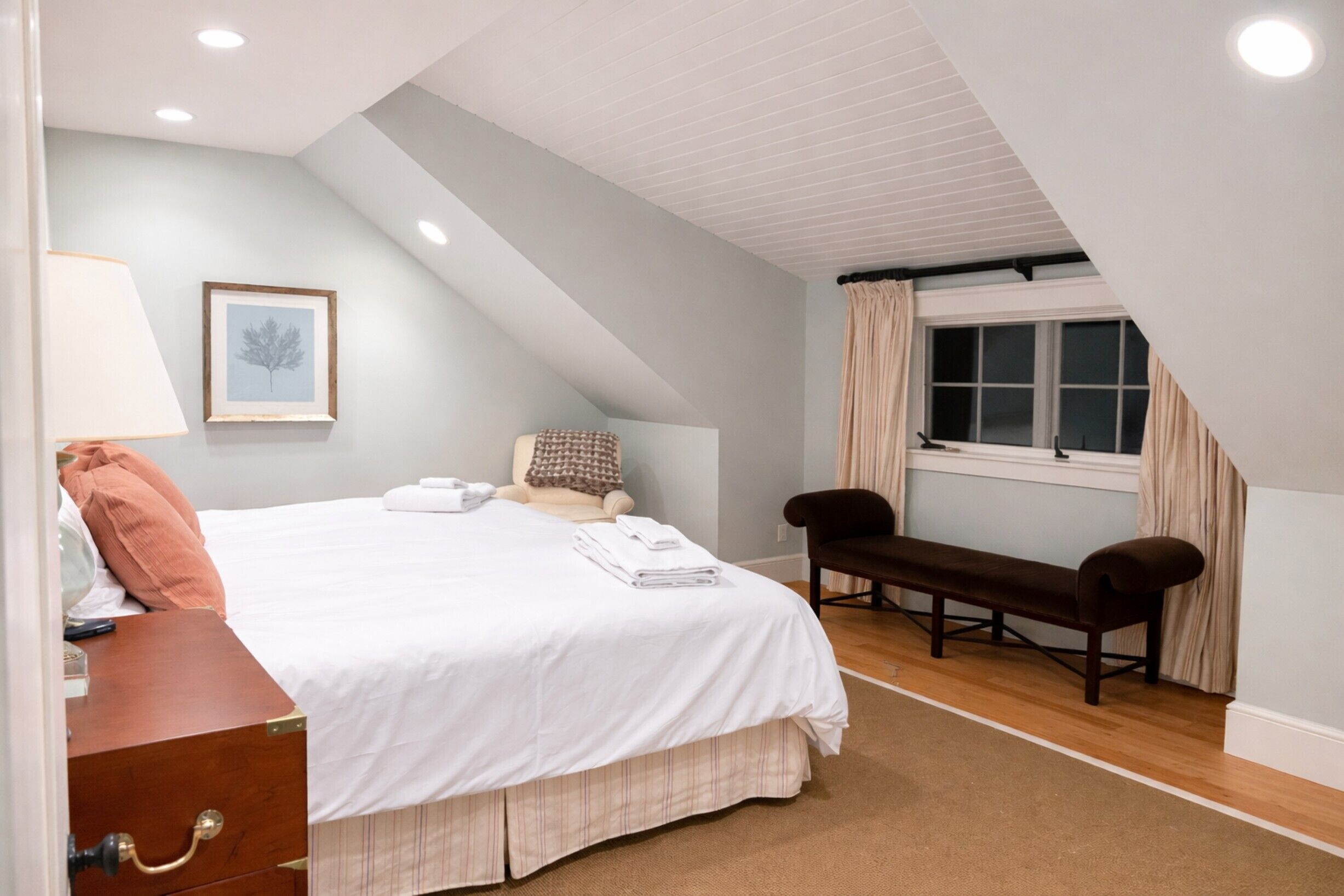 Un dormitorio con cama, un banco, una ventana y una lámpara.