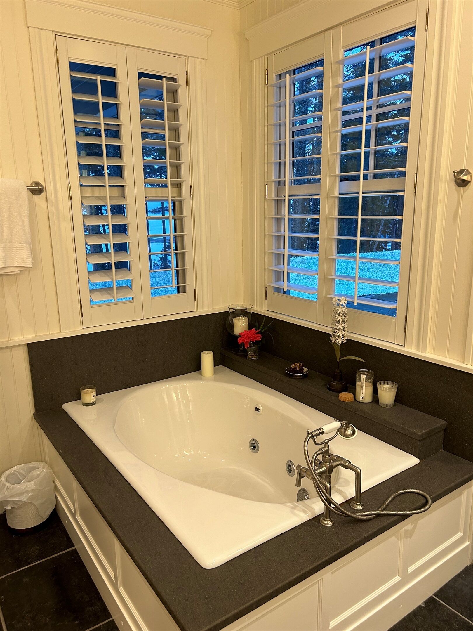 A bathroom with a large bathtub, white cabinetry, and a window with blinds.