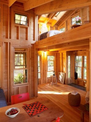 A cozy cabin interior with a loft bedroom, wooden floors, and large windows offering views of the outdoors. - Stunning, Private 35 Acre Oceanfront Retreat (Harpswell)