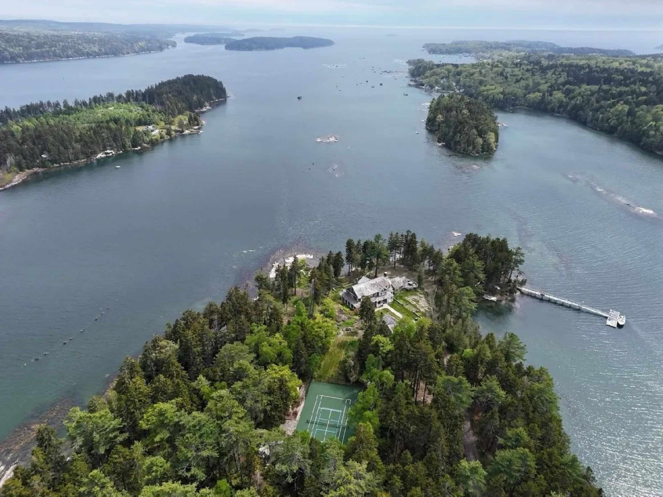 Vista aerea di un'isola isolata con campo da tennis circondato da fitta vegetazione, un molo e una piccola casa.