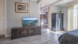 Een moderne woonkamer met een flatscreen televisie op een houten dressoir, een ingelijst schilderij aan de muur en uitzicht op een balkon.