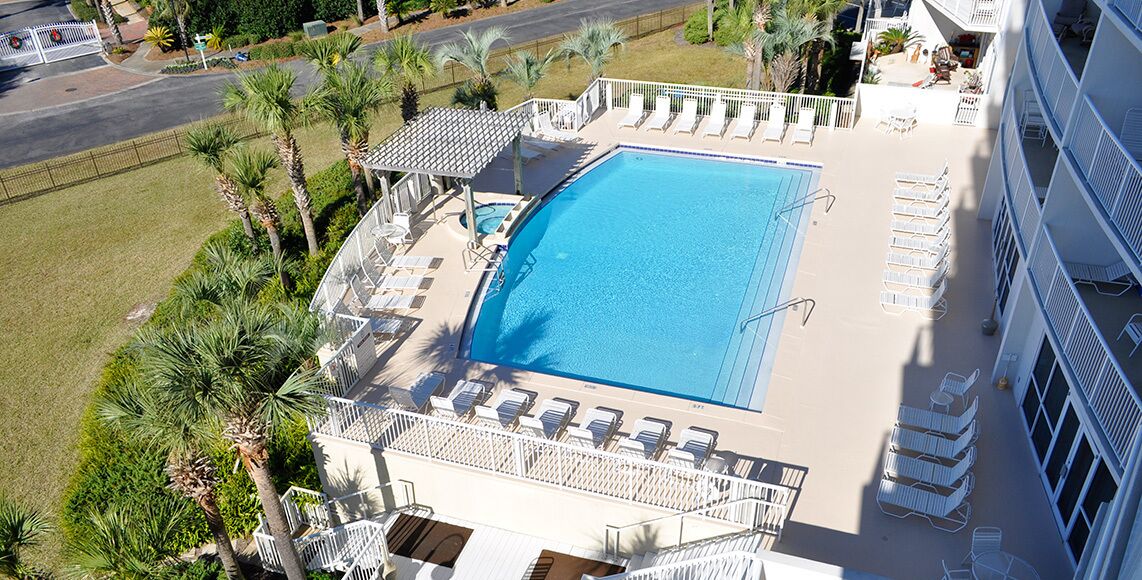Vue aérienne d’un hôtel doté d’une grande piscine, entourée de transats et de palmiers.