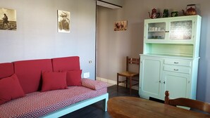 Una habitación con un sofá rojo estampado, una mesa de comedor de madera y un mueble verde claro con objetos decorativos.