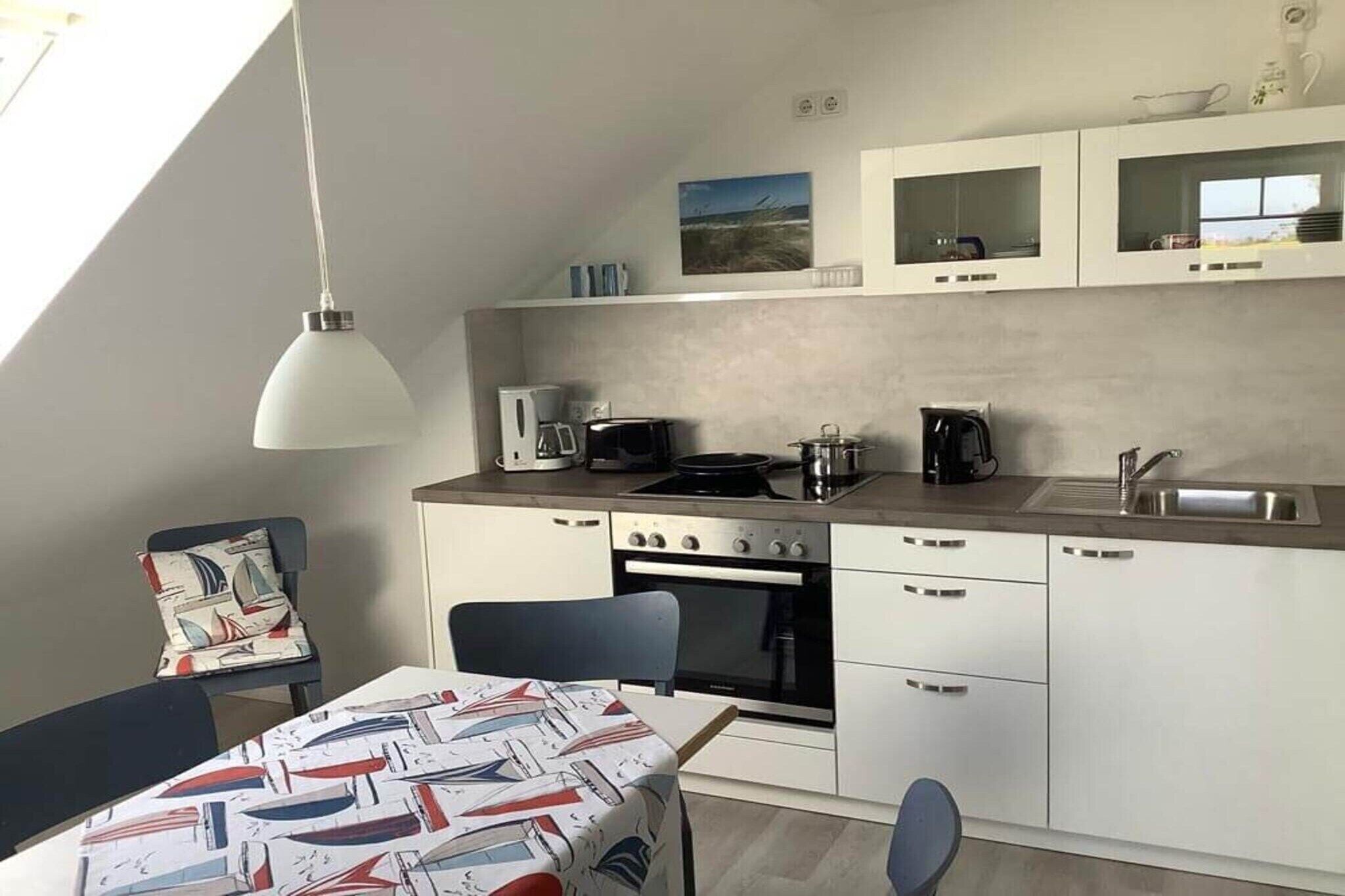 Una cocina moderna con zona de comedor, que incluye una mesa con mantel de temática náutica, una silla y una lámpara colgante.