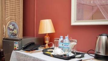 A hotel room with a desk, a telephone, a lamp, two bottles of water, a kettle, and a framed picture on the wall.