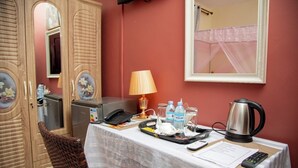 Een hotelkamer met een ontbijttafel, inclusief een waterkoker, theepot en ontbijtartikelen. Er is een telefoon, een lamp en een spiegel aan de muur.