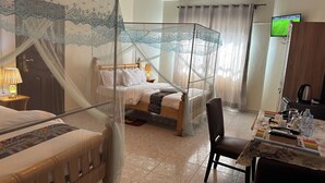 Een hotelkamer met een hemelbed, een losse zithoek, een eettafel met stoel en een televisie aan de muur.