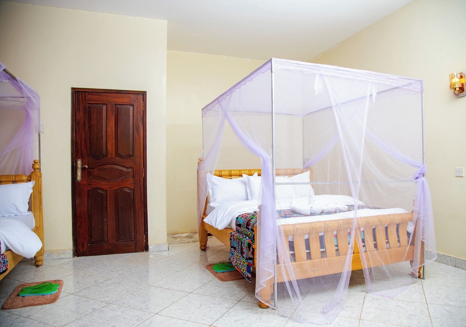 A room with a wooden bed with a canopy, a wooden door, and a tiled floor.