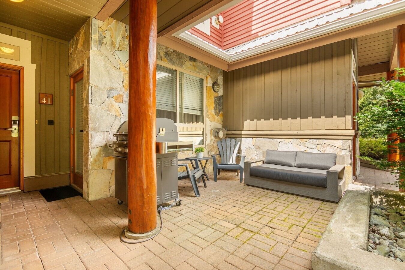 A covered outdoor area with a grill, seating, and a stone wall.
