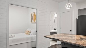 A modern, compact room with a bed, a small desk, and a bathroom. - Bright Whistler Village 1BR, HotTub, Free Parking, AC (Whistler)
