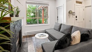 A modern living room with a grey sofa, a round coffee table, and a fireplace. - Bright Whistler Village 1BR, HotTub, Free Parking, AC (Whistler)