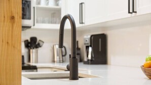 Une cuisine moderne avec un robinet noir élégant, des armoires blanches et un saladier en bois rempli de fruits posé sur le plan de travail.