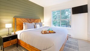 Une chambre avec une tête de lit en bois, une grande fenêtre, un téléviseur à écran plat et une table de chevet avec une lampe et un plateau contenant des articles pour le petit-déjeuner.