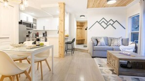Une cuisine moderne avec des meubles blancs, une table à manger avec des chaises et un mur d’accent en bois.