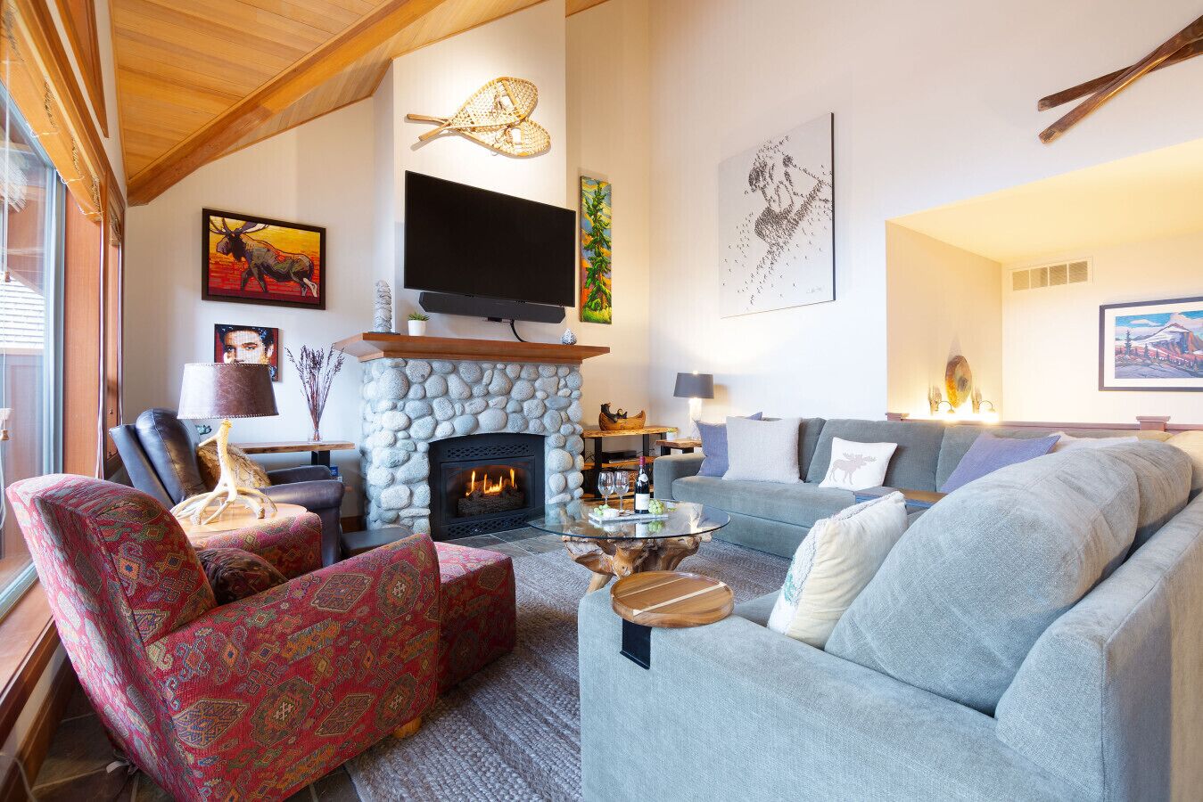 Ein gemütliches Wohnzimmer mit Kamin aus Stein, einem darüber montierten Fernseher und einer komfortablen Sitzecke mit Sofa und Sesseln.