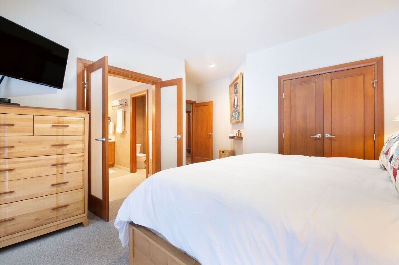 A bedroom with a large bed, wooden wardrobe, and a television on the wall.