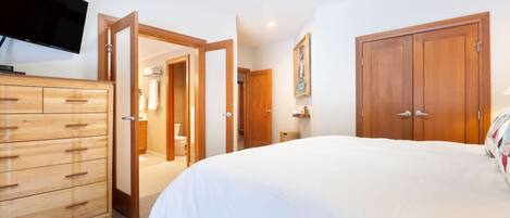 A bedroom with a large bed, wooden wardrobe, and a television on the wall.