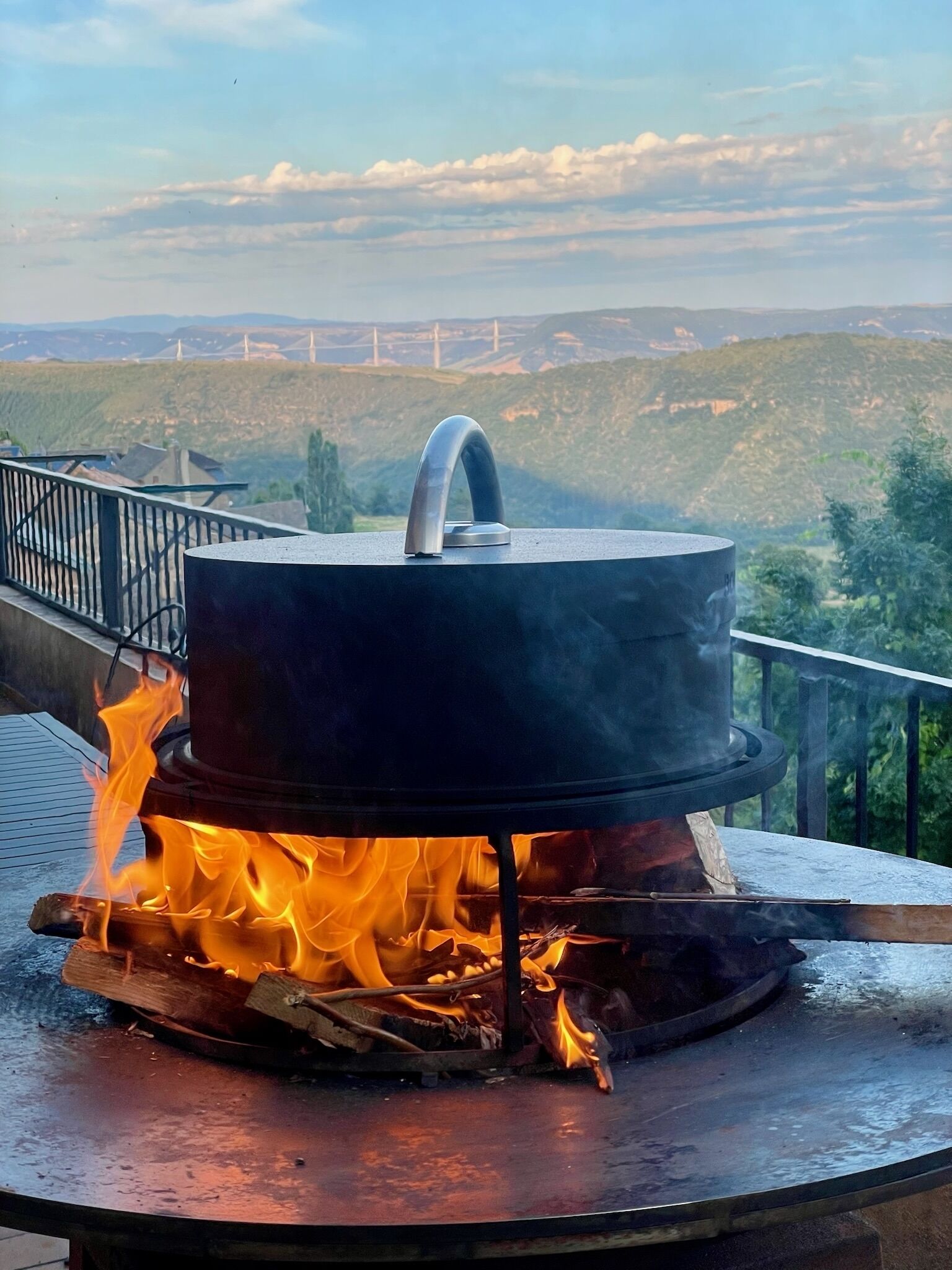 A portable stove with a pot on a balcony overlooking a hilly landscape.