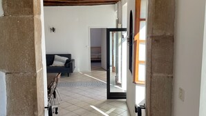 Un passage encadré de pierres mène à une pièce dont le sol est recouvert de carreaux, et qui contient un canapé et une table à manger.