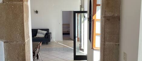 Un vano de puerta enmarcado en piedra que da a una habitación con suelo de baldosas, un sofá y una mesa de comedor.