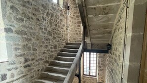 Un escalier en pierre, dans un bâtiment au décor rustique, mène à une fenêtre grillagée.
