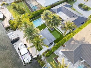 An aerial view of a residential property with a swimming pool, a covered outdoor area, and a dock with a boat. - Beautiful views of Naples Bay and walking distance to 5th ave! (Naples)