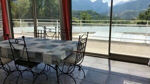 A dining area with a table set for four, large windows with a view of mountains and a lake, and a balcony with a railing.