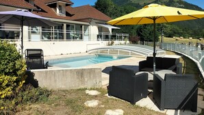 A pool area with outdoor furniture, a glass balustrade, and a mountain backdrop.