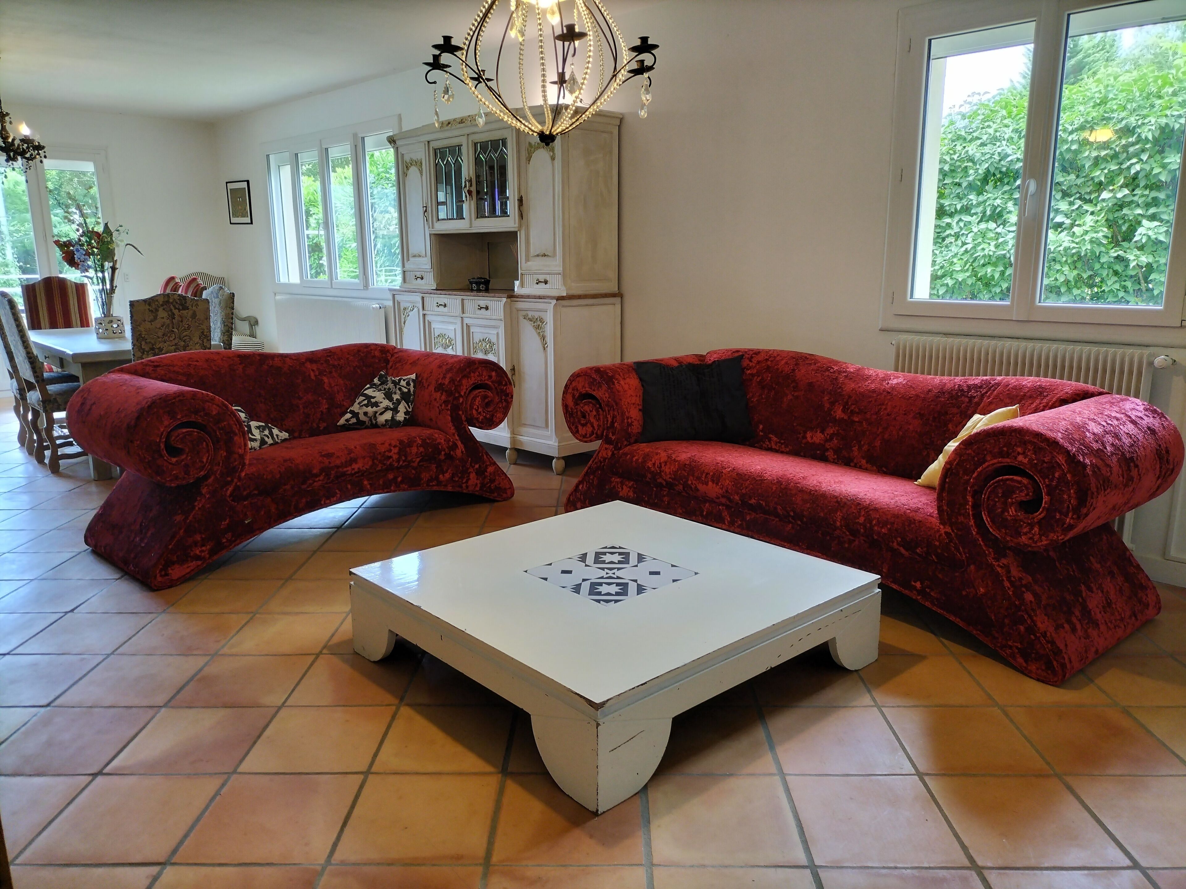 A living room with two red velvet sofas, a white coffee table, and a chandelier.