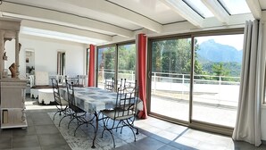 A dining area with a table and chairs, large windows with a view of mountains, and a balcony with a railing.