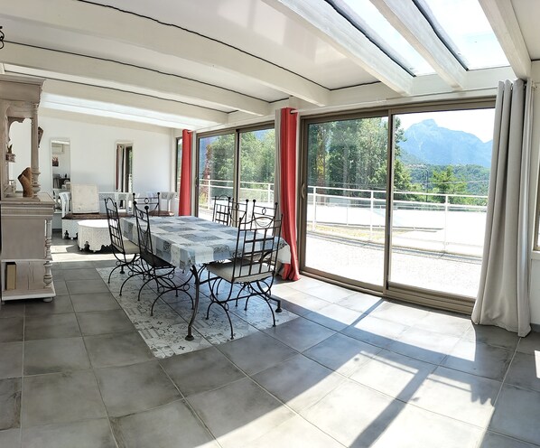 A dining area with a table and chairs, large windows with a view of mountains, and a balcony with a railing.