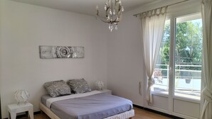 A bedroom with a bed, a chandelier, a window with curtains, and a view of greenery outside.