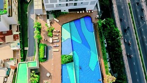 An aerial view of a modern building with a rooftop pool, surrounded by greenery and a road. - Cen Oasis Apart - CenRiver Side (Ho Chi Minh City)