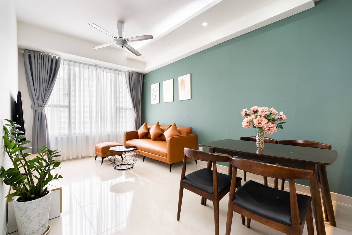 A modern living room with a sofa, dining table, chairs, a ceiling fan, and a potted plant.