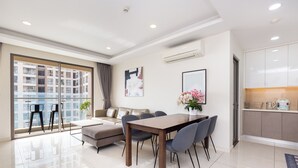A modern living room with a dining table, sofa, and chairs. There is a large window with a view of buildings. - Cen Oasis Apart - CenRiver Side (Ho Chi Minh City)