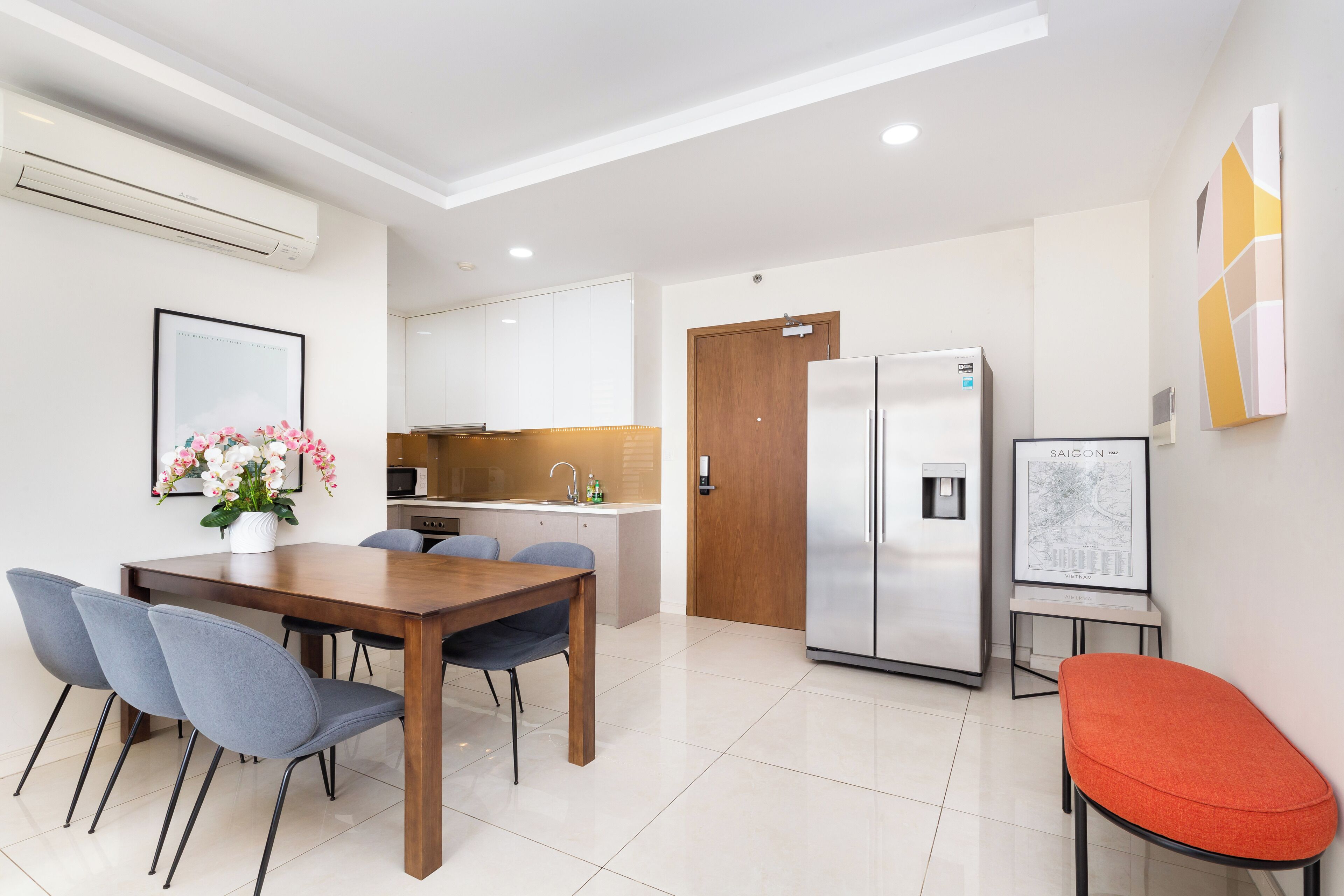 A modern kitchen with white cabinets, a stainless steel refrigerator, and a dining area with a wooden table and chairs.