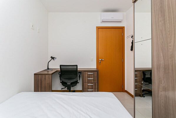 A bedroom with a bed, a desk with a chair, a wardrobe, and a door.
